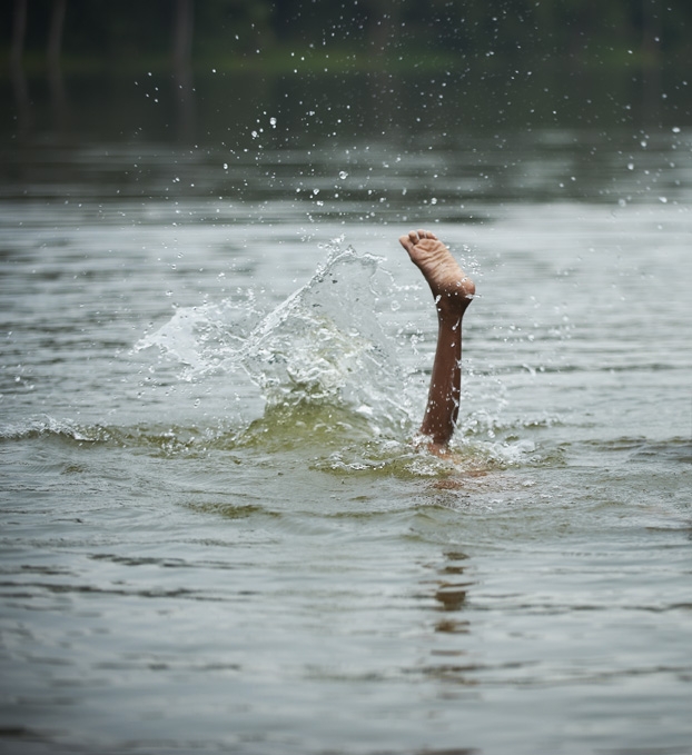Boy playing in river in Cambodia. Foot sticking out of water.