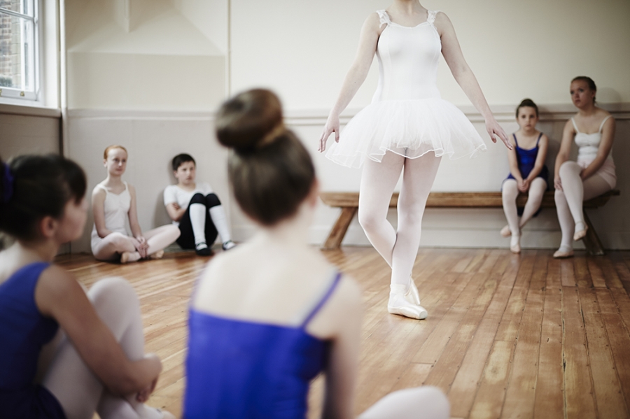 Ballet pupils sit around a performing fellow pupil in class.