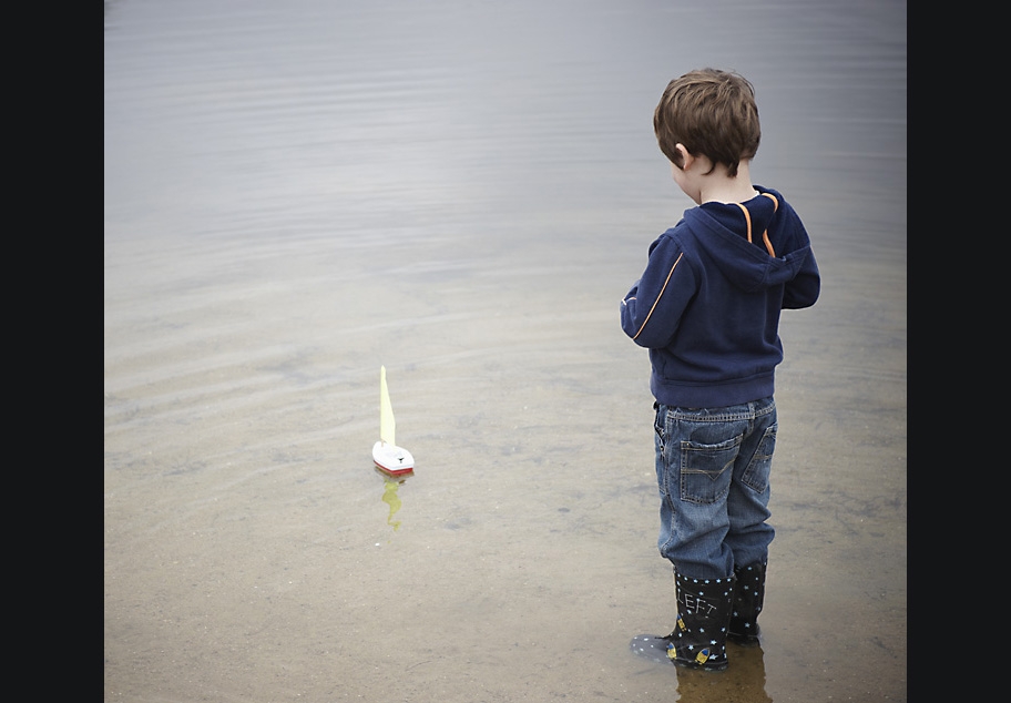Young boy sailing toy boat on pond