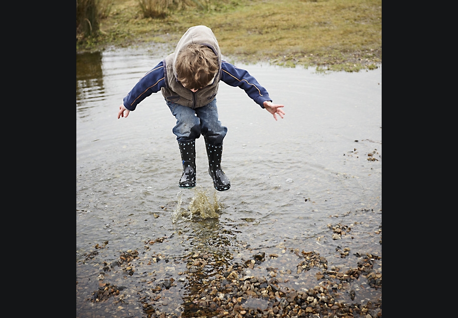 Young boy jumping huge puddle