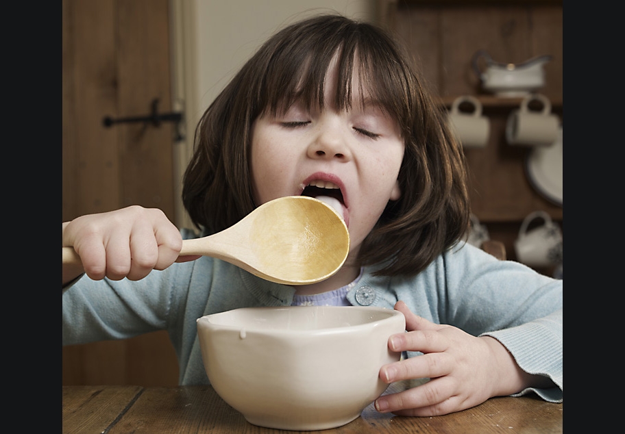 Young girl licking cake mixture off wooden spoon
